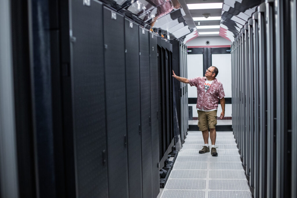 man walking through hallway of servers in data center